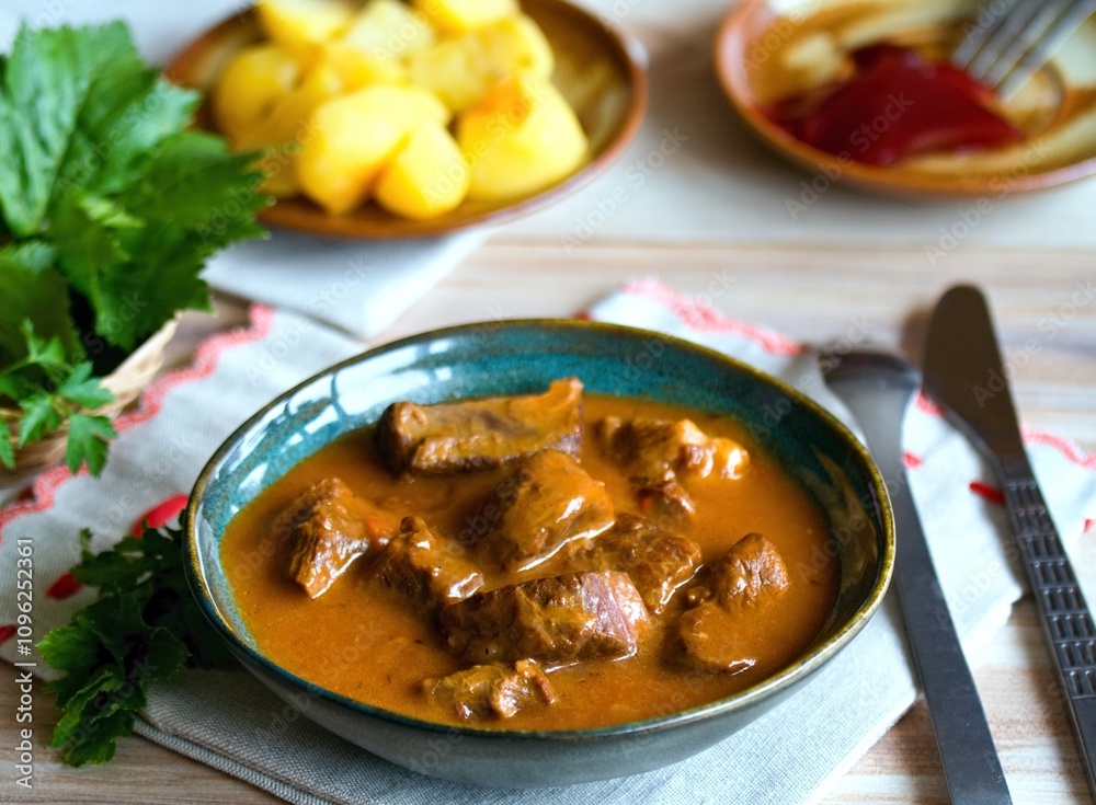 Delicious goulash made from deer meat in a bowl. Game stew with potatoes and red currant jam in a back. Delicious goulash made from deer meat in a bowl. Game stew with potatoes and red currant jam in a back.