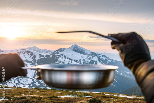 Travel concept and background. Defocused hands holding a tourist frying pan against the backdrop of snowy mountains, with Hoverla in focus at sunset. photo