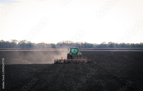 A powerful tractor plows a fertile field, raising clouds of dust against a clear blue sky, symbolizing hard work in agriculture and the beauty of rural life and industriousness of farmers