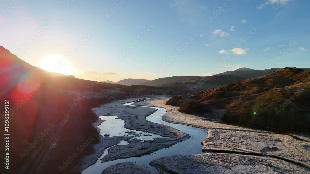Vídeo aéreo de um lago congelado na Escócia durante o pôr do sol, destacando a beleza das águas congeladas, o brilho dourado e a serenidade da paisagem ao entardecer