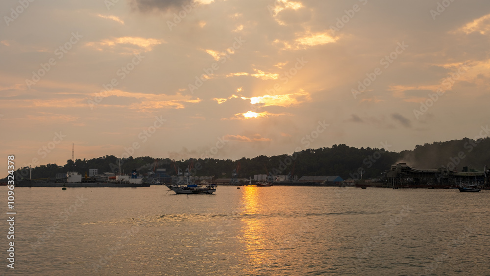 The afternoon atmosphere at a port in Indonesia, with an industrial area in the background. Fishing boats are docked on the shore, reflecting a blend of local maritime activity and industrial The afternoon atmosphere at a port in Indonesia, with an industrial area in the background. Fishing boats are docked on the shore, reflecting a blend of local maritime activity and industrial