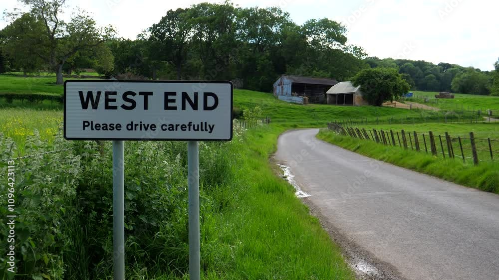 West End place name roadside plate sign by the road in countryside, farm building, static shot. West End place name roadside plate sign by the road in countryside, farm building, static shot.