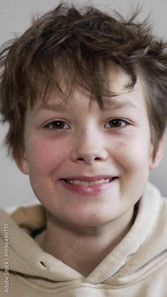 Smiling brunet Caucasian boy portrait. Teenager in hoodie shows his teeth looking into camera. Close up. Vertical video
