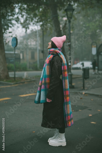 A woman in a pink hat and colorful scarf stands on the street