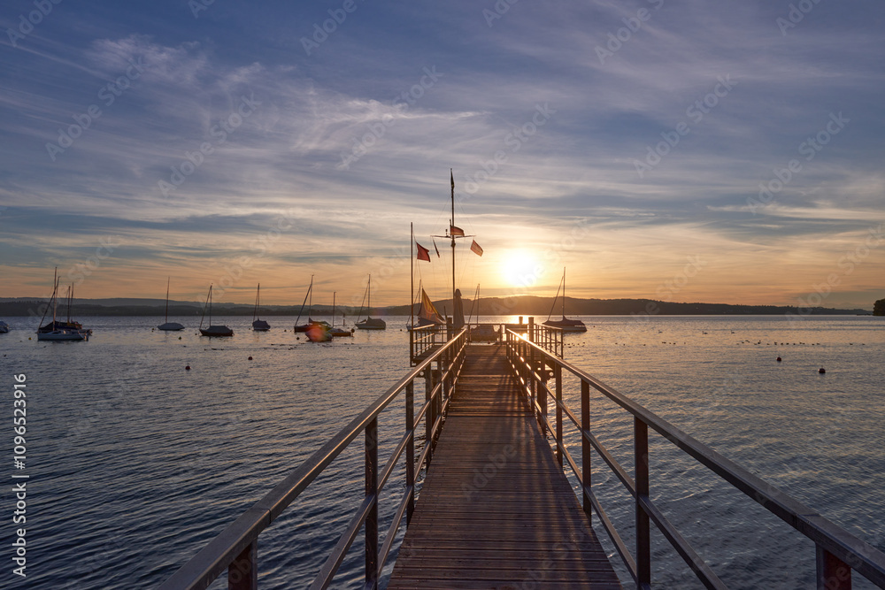 A serene sunset over a calm river, with vibrant orange and pink hues in the sky. A small sailboat is anchored in the water, reflecting the colorful sky. A serene sunset over a calm river, with vibrant orange and pink hues in the sky. A small sailboat is anchored in the water, reflecting the colorful sky.