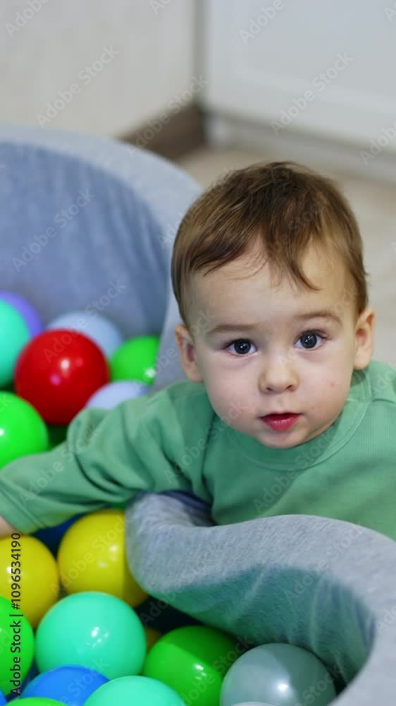 Lovely kid plays at the dry pool filled with colorful toys. Small child plays indoors. Top view. Vertical video Lovely kid plays at the dry pool filled with colorful toys. Small child plays indoors. Top view. Vertical video