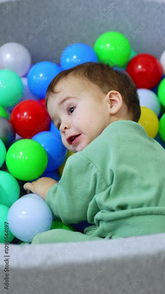Active cute Caucasian boy playing in the balls of dry pool. Lovely boy lies down on the toys. Top view. Vertical video Active cute Caucasian boy playing in the balls of dry pool. Lovely boy lies down on the toys. Top view. Vertical video