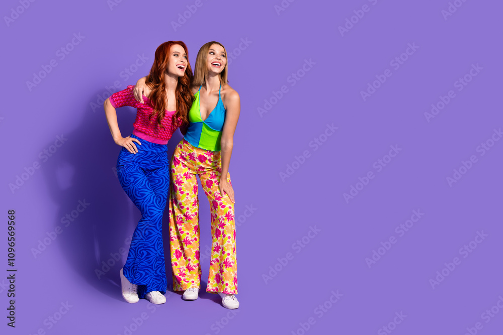 Full length portrait of two nice stunning girls cuddle look empty space isolated on purple color background Full length portrait of two nice stunning girls cuddle look empty space isolated on purple color background