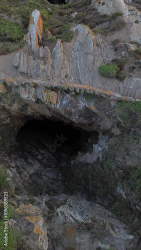 Aerial view of Ons Island's Burato do Inferno, a deep cavern descending to the sea, bordered by stone wall and surrounded by lush vegetation. The Atlantic waters are visible at the end of the cavern. photo