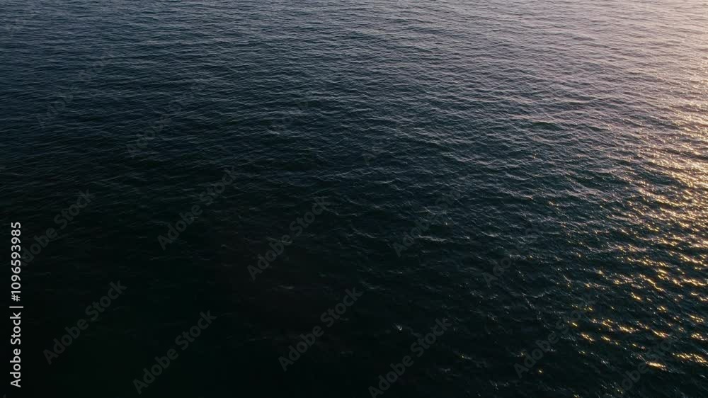 Aerial view of soft morning light glimmers on tranquil ocean waters, creating a serene atmosphere with gentle waves lapping against each other