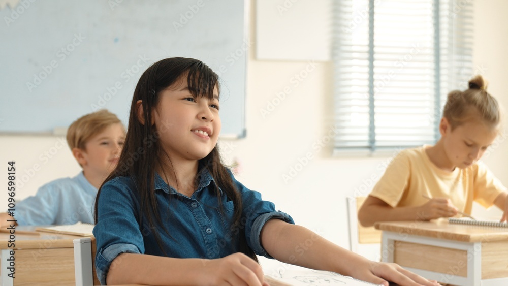 Smart elementary student looking at teacher while attend in classroom. Diverse smart student sitting at classroom while listening teacher explain about classwork or test. Education concept. Pedagogy.