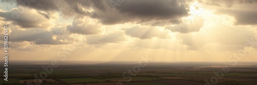 Rays of sunshine pierce through holes in greyish-brown clouds illuminating a patchwork quilt of green and brown hues on the ground, earthy tones, landscape photography, sunny day