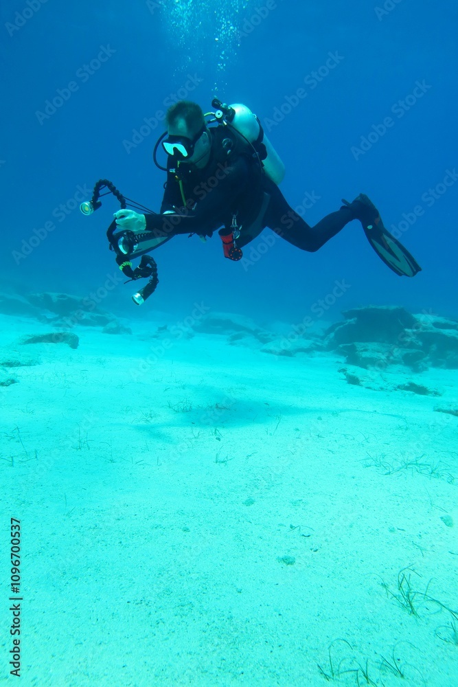 Scuba diver photographer swimming free in the ocean, blue seascape. Deeper seascape with the sand and stones and swimming underwater photographer. Travel picture, exploration scuba trip. Sea and diver Scuba diver photographer swimming free in the ocean, blue seascape. Deeper seascape with the sand and stones and swimming underwater photographer. Travel picture, exploration scuba trip. Sea and diver
