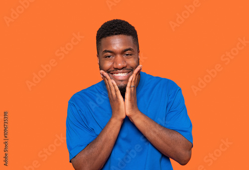 Smiling young man in blue shirt expressing joy against orange background