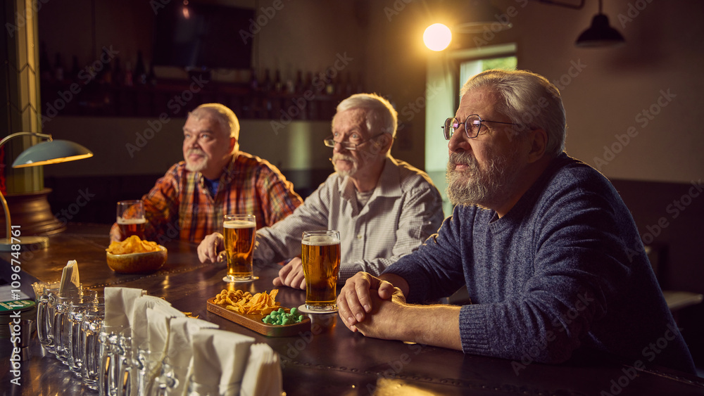 Three elderly man sitting at bar with beer and chips snacks, watching game translation with attention, supporting favorite team. Concept of sport fans, elderly lifestyle, leisure activity, emotions Three elderly man sitting at bar with beer and chips snacks, watching game translation with attention, supporting favorite team. Concept of sport fans, elderly lifestyle, leisure activity, emotions