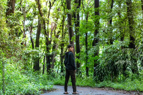 Young man standing alone while watching you. Beautiful dramatic deep forest greenery