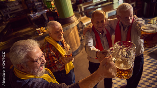 Top view of elderly men clinking mugs with lager beer. Friends gathering in modern pub, drinking beer and watching game translation.. Concept of sport fans, elderly lifestyle, leisure activity