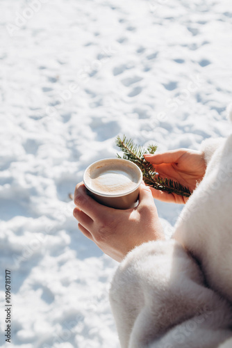 A paper cup of cappuccino in a female hand in winter, close up.