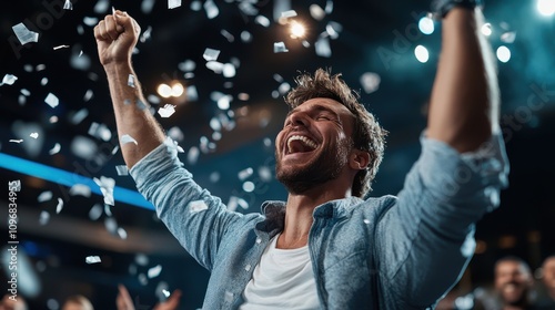 A jubilant man in a blue shirt laughs and celebrates with raised arms as white confetti showers him in a scene filled with joy and exuberant energy. photo