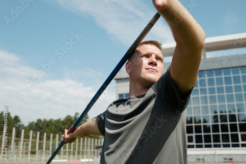 Athlete holding javelin on athletic track with modern building visible in the background, preparing for or resting after practice session photo