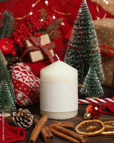 Pillar candle with label near red knitted sweater and Christmas decor and lights, winter mockup