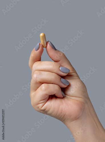 Female hand holding a yellow capsule with fingers closeup against grey, Healthcare concept