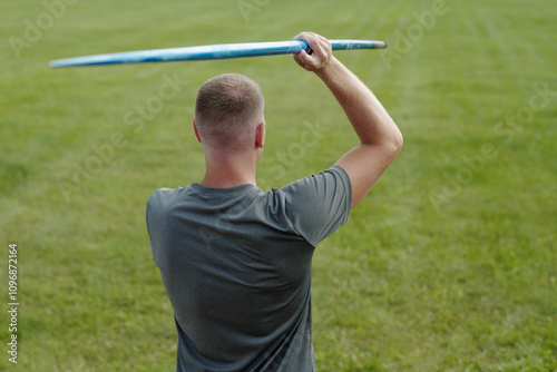 Man standing on open grassy field throwing frisbee with extended arm. Wearing casual grey t-shirt enjoying recreational activity on bright day photo