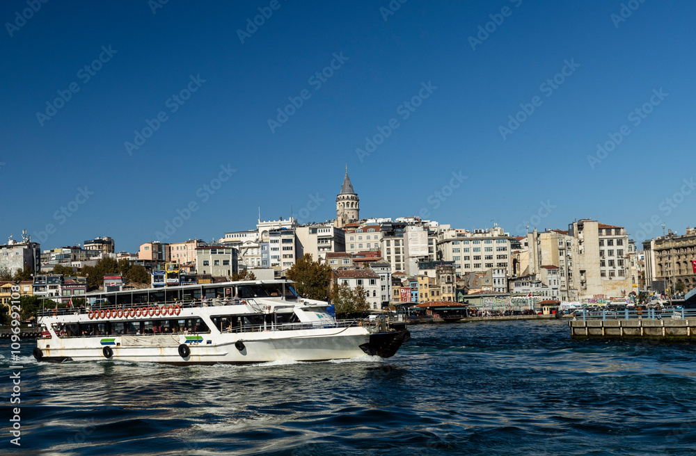 Fototapeta premium A picturesque view of the Bosphorus with the white ferry gliding across the calm waters with the iconic Galata Tower visible in the background a symbol of Istanbul's rich history and cultural heritage