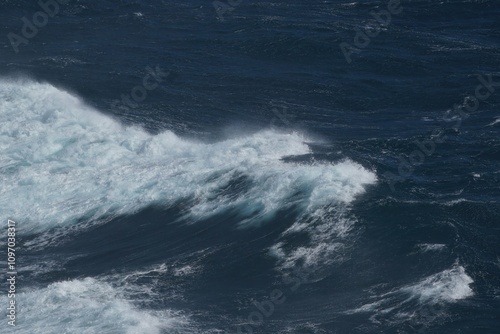 Waves crashing on dark ocean surface create dynamic and powerful scene. contrast of white foam against deep blue water evokes sense of nature raw energy and beauty