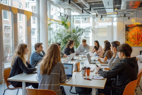 People are engaged in discussion around a large conference table, brainstorming ideas on laptops