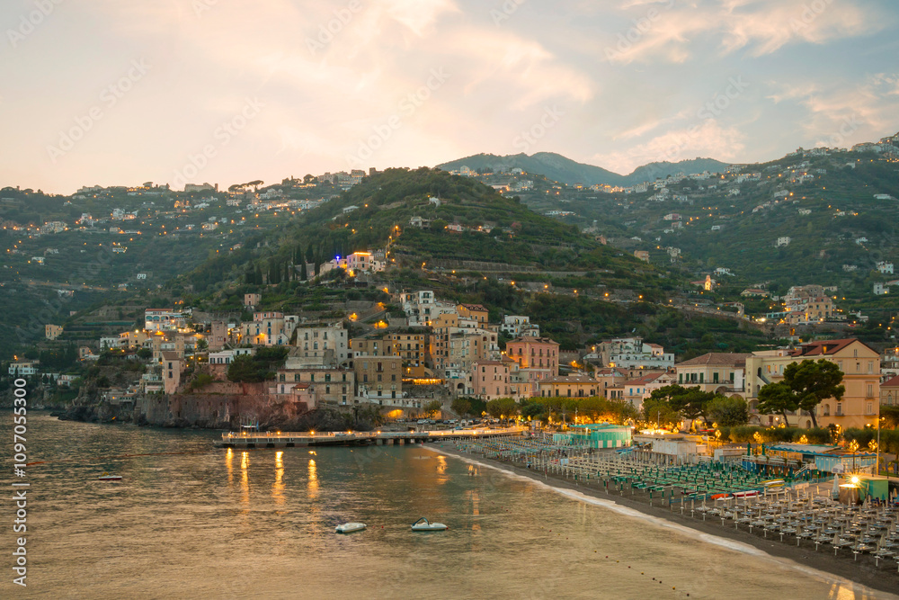 This image showcases Minori on the Amalfi Coast, with its charming seaside houses, tranquil beach, and lush green hills, bathed in the warm Mediterranean light.