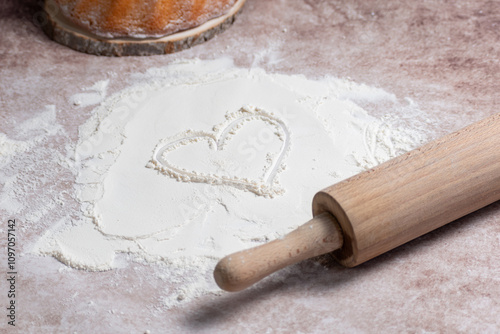 Heart drawn on spilled flour, love for baking, kitchen background,Roller with flour and ready-made dough on a brown background, photo