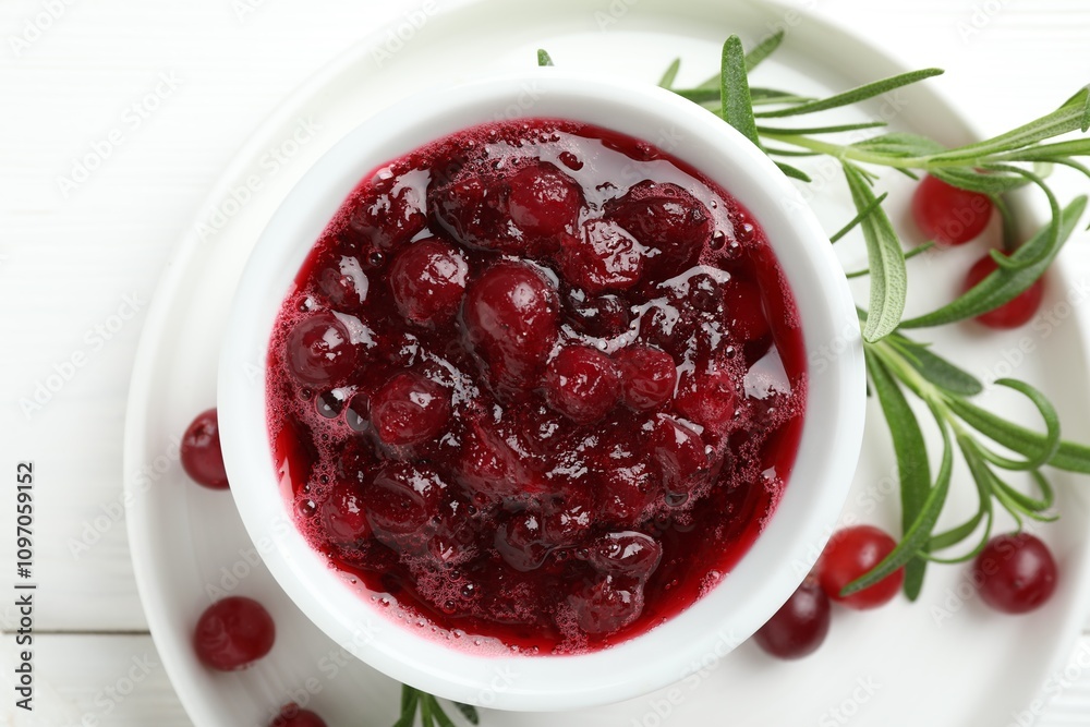Tasty cranberry sauce in bowl, berries and rosemary on white table, top view Tasty cranberry sauce in bowl, berries and rosemary on white table, top view