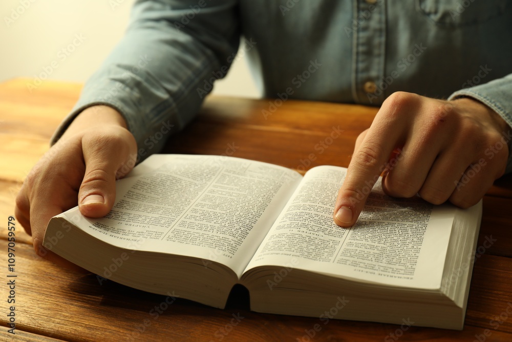 Man reading Holy Bible in English language at wooden table, closeup Man reading Holy Bible in English language at wooden table, closeup