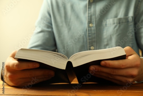 Man reading Holy Bible at wooden table, closeup