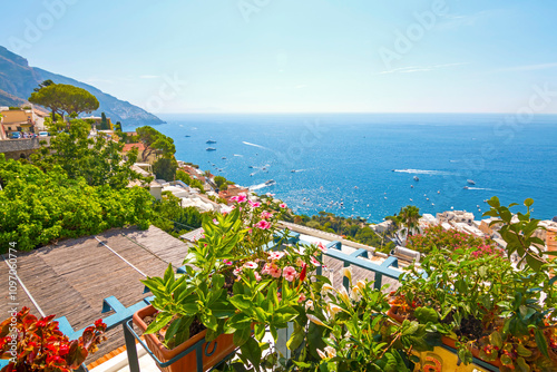 The photo captures a view of Positano, with its colorful, stacked houses cascading down the cliffs, narrow winding streets, and vibrant coastline set against the clear blue sea and sky