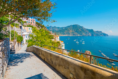 Obraz na płótnie The photo captures a sunny view of Amalfi, showcasing the town's colorful buildings, steep cliffs, and vibrant coastline under a clear blue sky on a bright day. w salonie