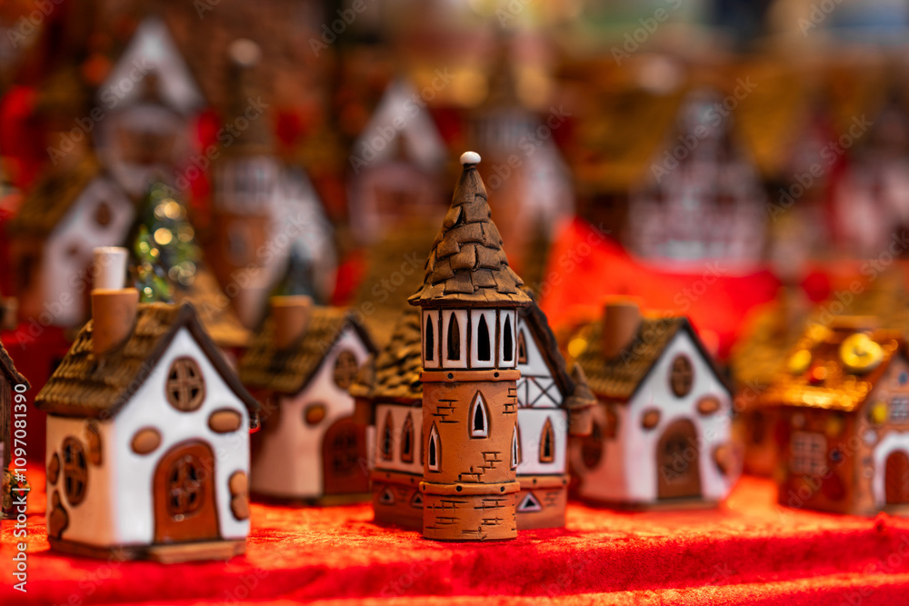 Fototapeta premium Detailed ceramic miniature houses and tower, arranged on red cloth display, creating cozy and festive village scene