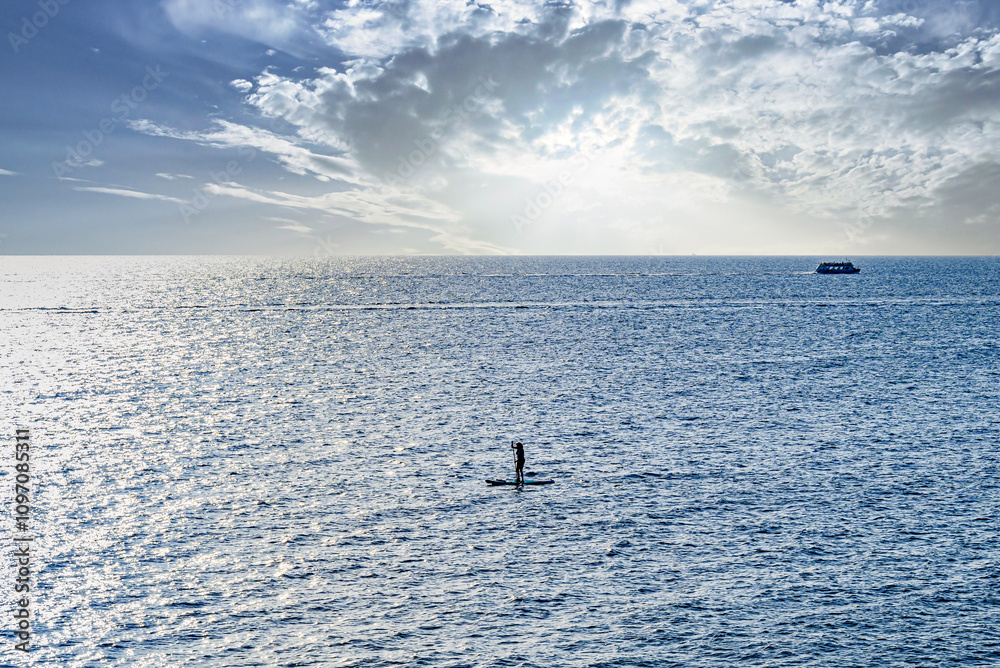 Obraz premium Silhouette of a woman practicing paddle surfing in the sea of ​​Menorca at sunset. Balearic Islands 