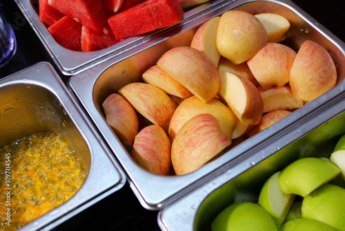 Assorted fresh fruits neatly arranged in stainless steel containers.