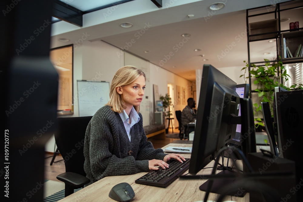 Focused woman working at dual monitors in modern office setting Focused woman working at dual monitors in modern office setting