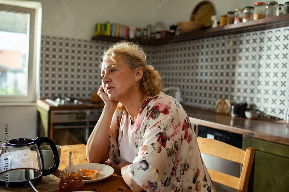 Thoughtful woman sitting at kitchen table during breakfast Thoughtful woman sitting at kitchen table during breakfast