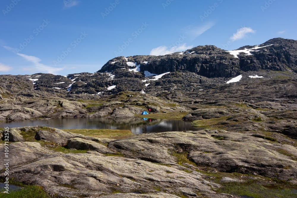Landscape with clear water lake on trail to Trolltunga, Norway, unrecognizable people making tent Landscape with clear water lake on trail to Trolltunga, Norway, unrecognizable people making tent