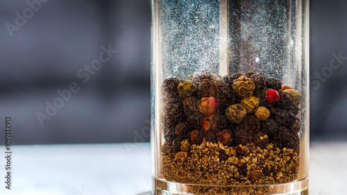 Close-up section of a glass peppermill with fresh and ground mixed peppers photo