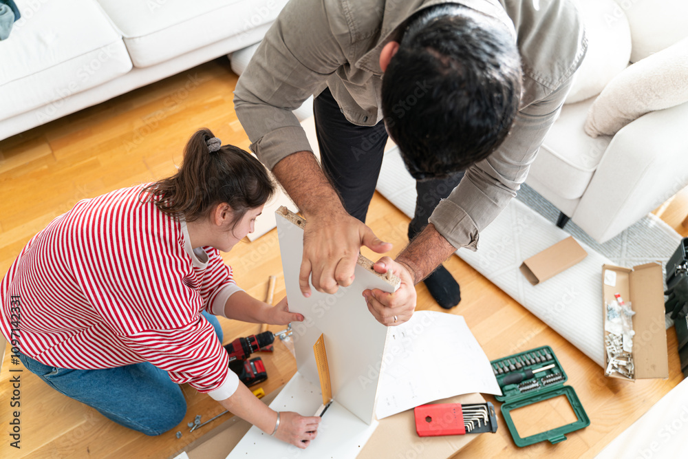 Happy Couple Assembles Furniture as a Team, Girl Reads Instructions and Boy Tightens Screw with a Drill. Moving into New Apartment, Couple Assemble Shelf.