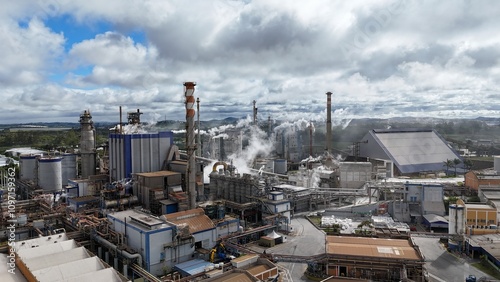 Aérea de uma indústria de papel e celulose, com chaminés emitindo fumaça, caldeiras em funcionamento e maquinário industrial operando em área cercada por natureza