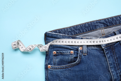 Jeans and measuring tape on light blue background, top view. Space for text photo