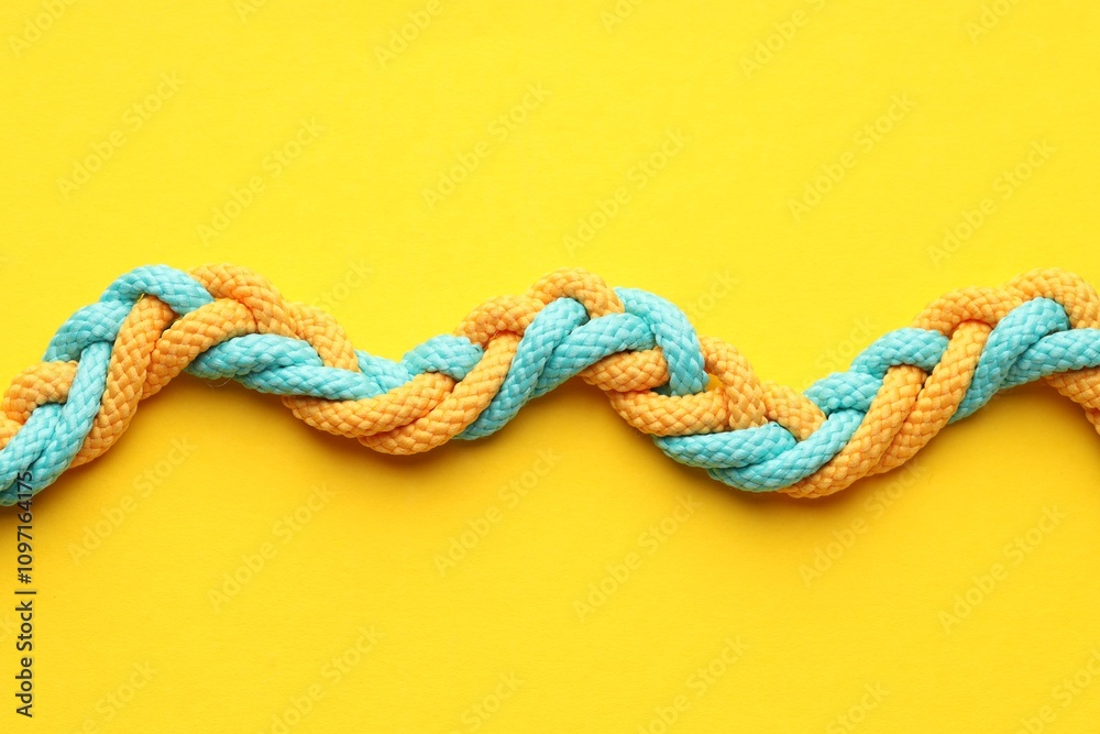 Colorful ropes tied together on yellow background, top view. Unity concept Colorful ropes tied together on yellow background, top view. Unity concept