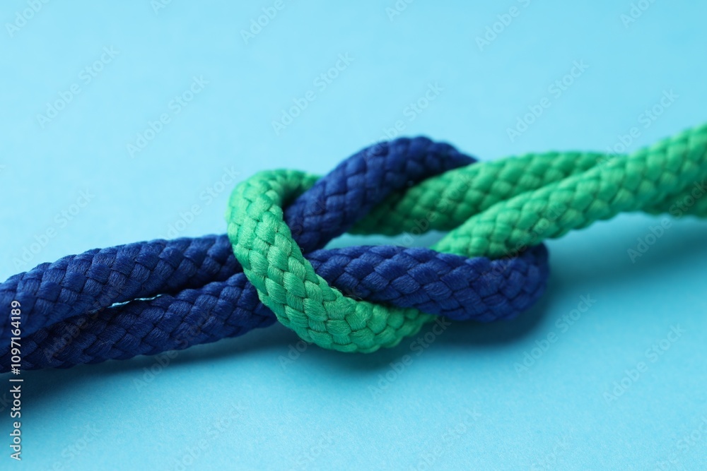 Colorful ropes tied in knot on light blue background, closeup. Unity concept Colorful ropes tied in knot on light blue background, closeup. Unity concept