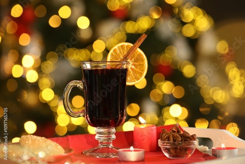 Aromatic mulled wine in glass cup, anise, cookies and burning candles on tray against blurred Christmas lights, bokeh effect